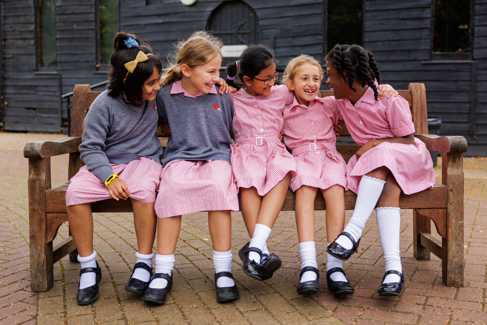 Group of Prep School Girls chatting together on a bench wearing a pink school uniform